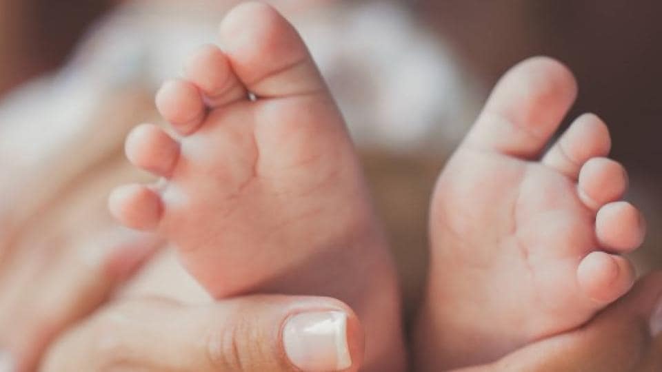 Close-up of a pair of baby feet held gently by an adult's hands against a blurred background.